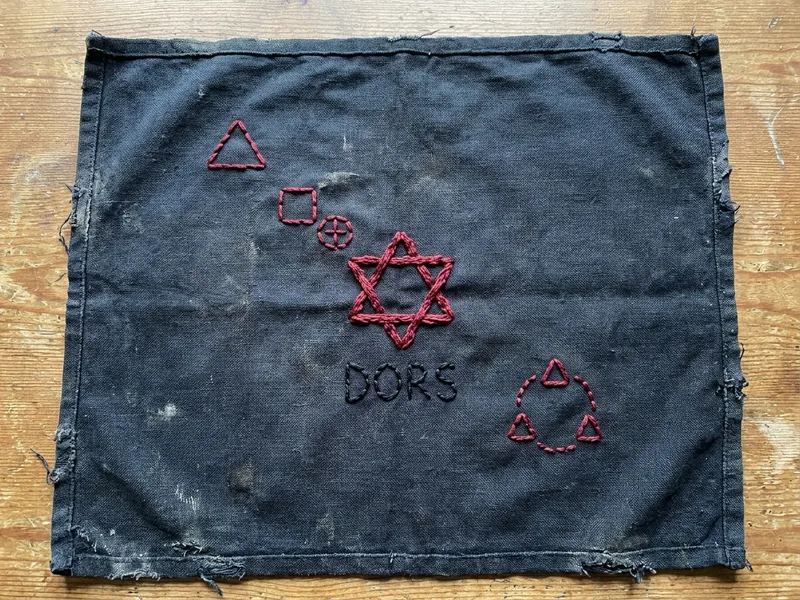 Carte brodée au fil rouge sur tissu bleu-noir, plan stylisé du mont Cagire, hameau, chapelle wisigothe, étoile rouge à six branches marquant la Porte, mot DORS brodé